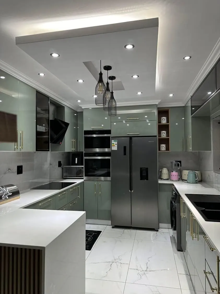 Sage green kitchen with pendant lights and tall units
